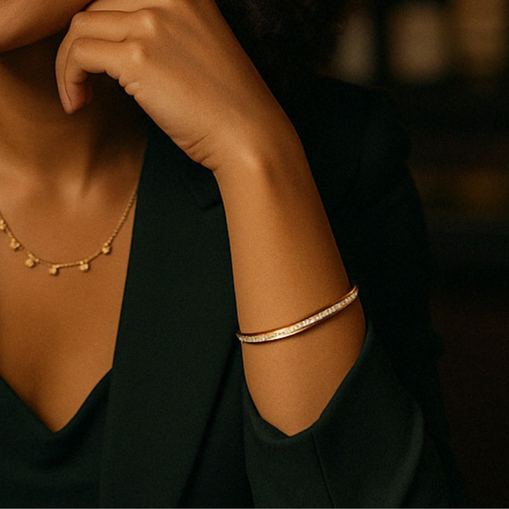 Close-up of a person wearing gold jewelry including a necklace and bracelet against a dark background.