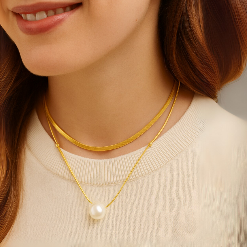 Close-up of a person wearing a gold necklace with a pearl pendant.
